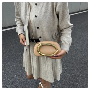 Close-up of minimalist beige leather crossbody bag with oval gold hardware and chain strap