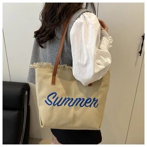 Detail of beige canvas tote with blue Summer embroidery and brown leather handles