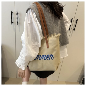 Detail of beige canvas tote with blue 'summer' embroidery and brown leather strap