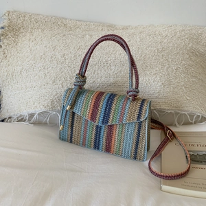 Detail of colorful woven straw bag with adjustable strap on a minimalist white bedding