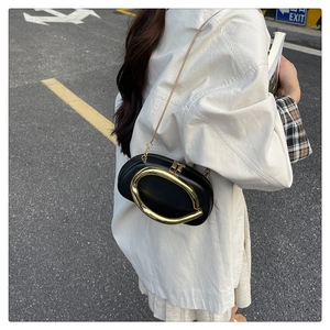 Detail of black oval crossbody bag featuring large gold ring hardware and metal chain strap