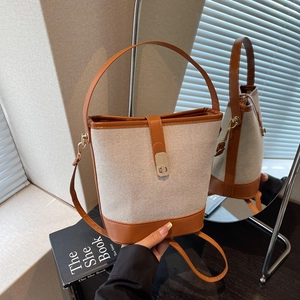 Retro bucket bag in cream canvas and brown leather with metal clasp on a reflective surface