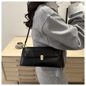 Detail of a black minimalist baguette bag with a gold metal clasp and sleek leather finish