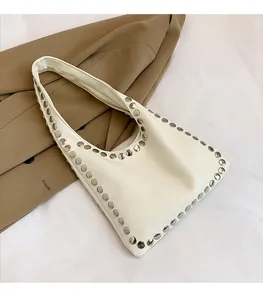 Detail of white leather shoulder bag featuring silver stud trim on khaki coat backdrop