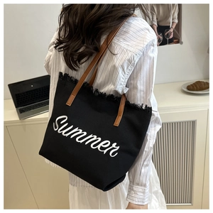 Close-up of black canvas tote with Summer embroidery and brown leather straps