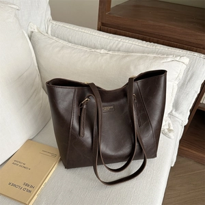 Large dark brown tote bag in vintage leather style with gold logo on a white pillow