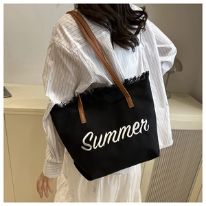 Detail of black canvas tote bag with Summer embroidery and fringe trim on shoulder
