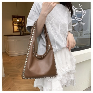 Detail view of the brown leather tote bag with silver rivets worn by a model in a street setting