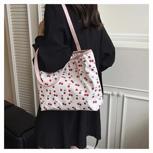 Détail du sac fourre-tout blanc à imprimé cerise et anses roses porté par un mannequin