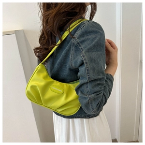 Close-up of bright green ruched crescent bag with embossed patch on denim jacket
