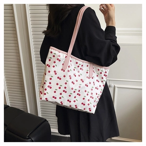 Close-up of a white tote bag featuring red cherry prints and pink shoulder straps