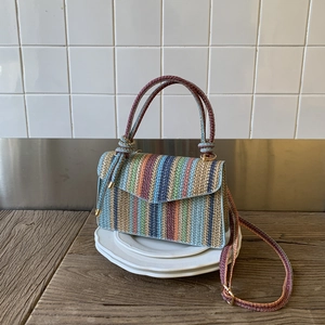 Colorful striped woven crossbody bag with top handle and gold hardware on white plates