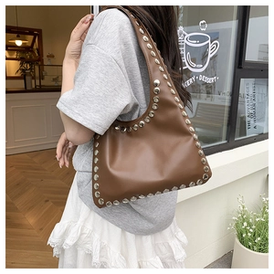 Detail of a brown leather shoulder bag featuring silver metal rivets in a cafe setting
