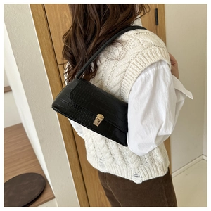 Detail view of black crocodile pattern shoulder bag with golden lock on female model