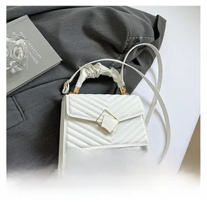 Close-up of white V-quilted small square bag with golden buckle on a grey blazer
