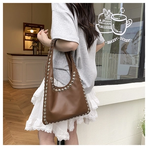 Close-up of brown leather shoulder bag featuring silver stud rivets on the edges