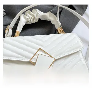 Detail of white quilted handbag with V-stitch texture and gold geometric buckle
