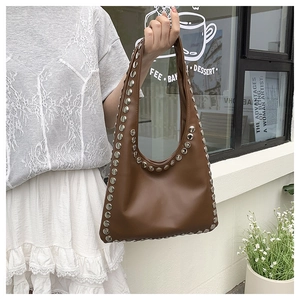 Close-up of brown leather hobo bag featuring large silver studs in a lifestyle setting