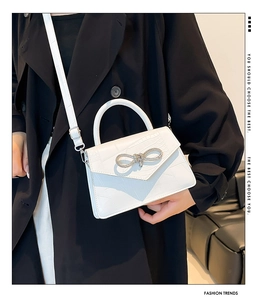 Detail of white croc-effect handbag with a sparkling rhinestone bow buckle and top handle