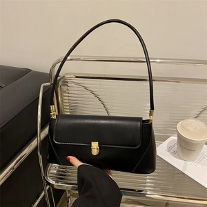 Minimalist black leather baguette bag with a gold buckle shown in a lifestyle city setting