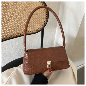 Detail of a brown crocodile pattern shoulder bag featuring a gold push-lock closure on a chair