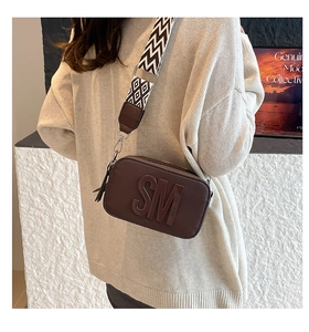 Détail du sac à bandoulière marron avec logo lettrage et large sangle géométrique