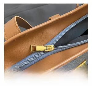 Close-up of golden hardware zipper and brown litchi texture leather on a tote bag