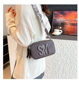 Gros plan du sac bandoulière en cuir marron avec logo embossé et sangle géométrique