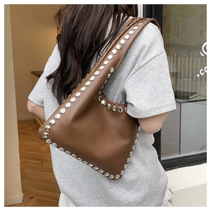 Detail of a brown leather tote bag featuring two rows of polished silver metal studs