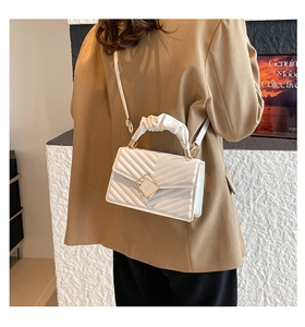 Detail of white quilted crossbody bag with golden lock and cloud-like pleated handle