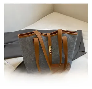 Detail of grey felt tote bag with brown leather trim and golden twist-lock closure