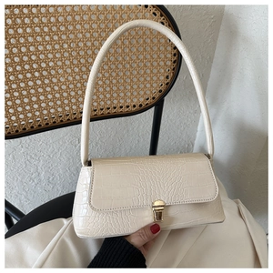 Detailed view of cream crocodile-embossed baguette bag with golden metallic clasp and strap