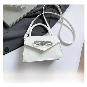 Detail of white crocodile pattern crossbody bag with rhinestone bow and phone for size
