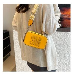 Détail du sac bandoulière rectangulaire jaune avec logo en relief et large sangle ondulée