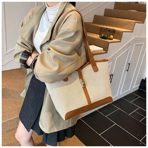 Detail of a large canvas tote bag with brown leather trim and golden metal clasp closure