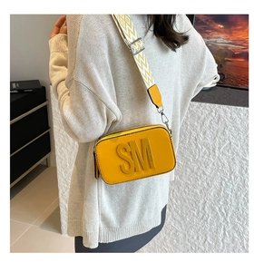 Détail d'un sac caméra jaune avec large bandoulière à motifs porté par un mannequin chic