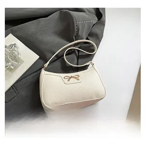 Detail of creamy white litchi leather underarm bag featuring a golden bow ornament