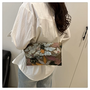 Detail of sequined envelope crossbody bag with floral embroidery and golden chain strap
