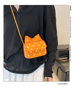 Orange polka dot shoulder bag with bow detail shown on model with black top