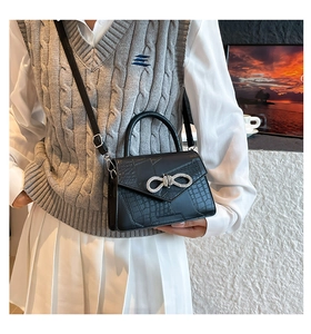 Detail of a black crocodile pattern handbag with a rhinestone bow on a female model