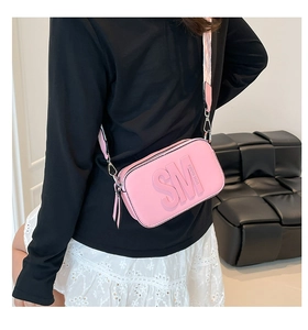 Sac bandoulière Steve Madden rose avec lettres gaufrées et sangle tissée porté par un modèle