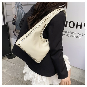 Detailed close-up of cream leather shoulder bag featuring silver rivets and punk style