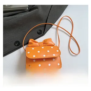 Detailed view of an orange polka dot crossbody bag featuring a decorative top bow