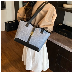 Close-up of a large grey canvas tote bag with black leather straps and a gold buckle