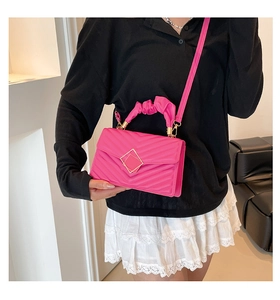 Detail of fuchsia quilted crossbody bag with gold buckle and pleated handle on a model