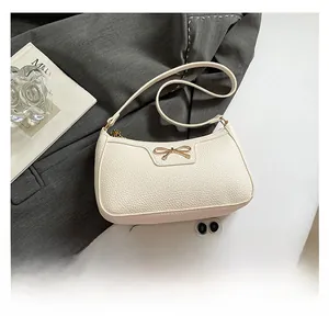 Close-up of cream lychee texture shoulder bag with golden metal bow and zipper detail