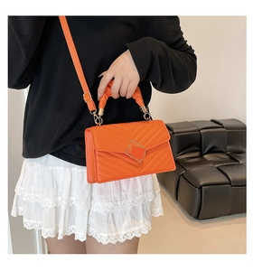 Detail view of orange V-quilted crossbody bag with gold buckle and pleated handle