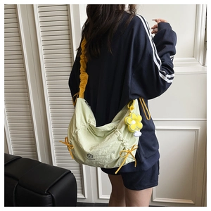 Detail of canvas messenger bag with yellow pleated strap and sunflower pendant