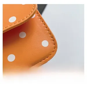 Detail showing high-quality orange leather texture with white polka dots and fine stitching