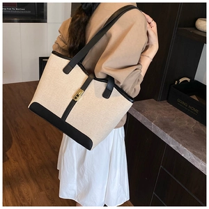 Detail of canvas tote bag with black leather trim and gold metal clasp on a model
